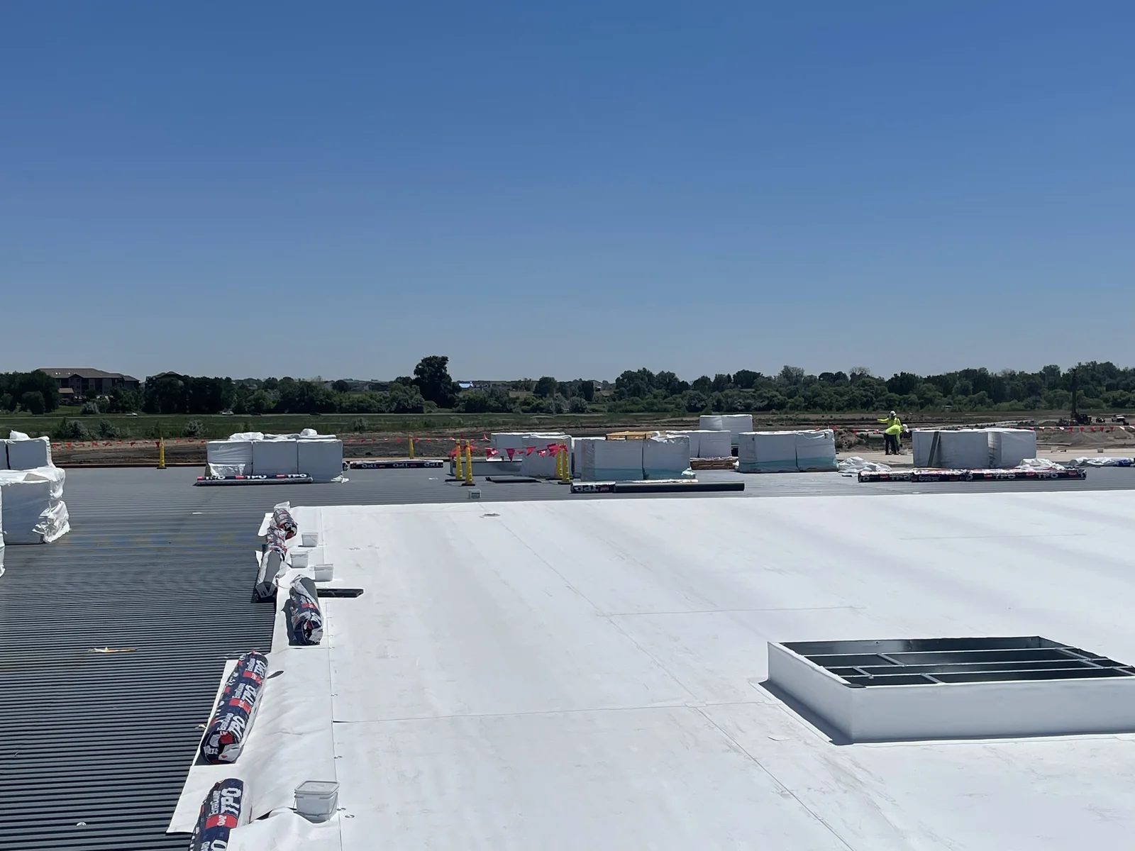 Wide commercial roof with white single-ply membrane, staged roofing materials, walkway surface, and rooftop curb