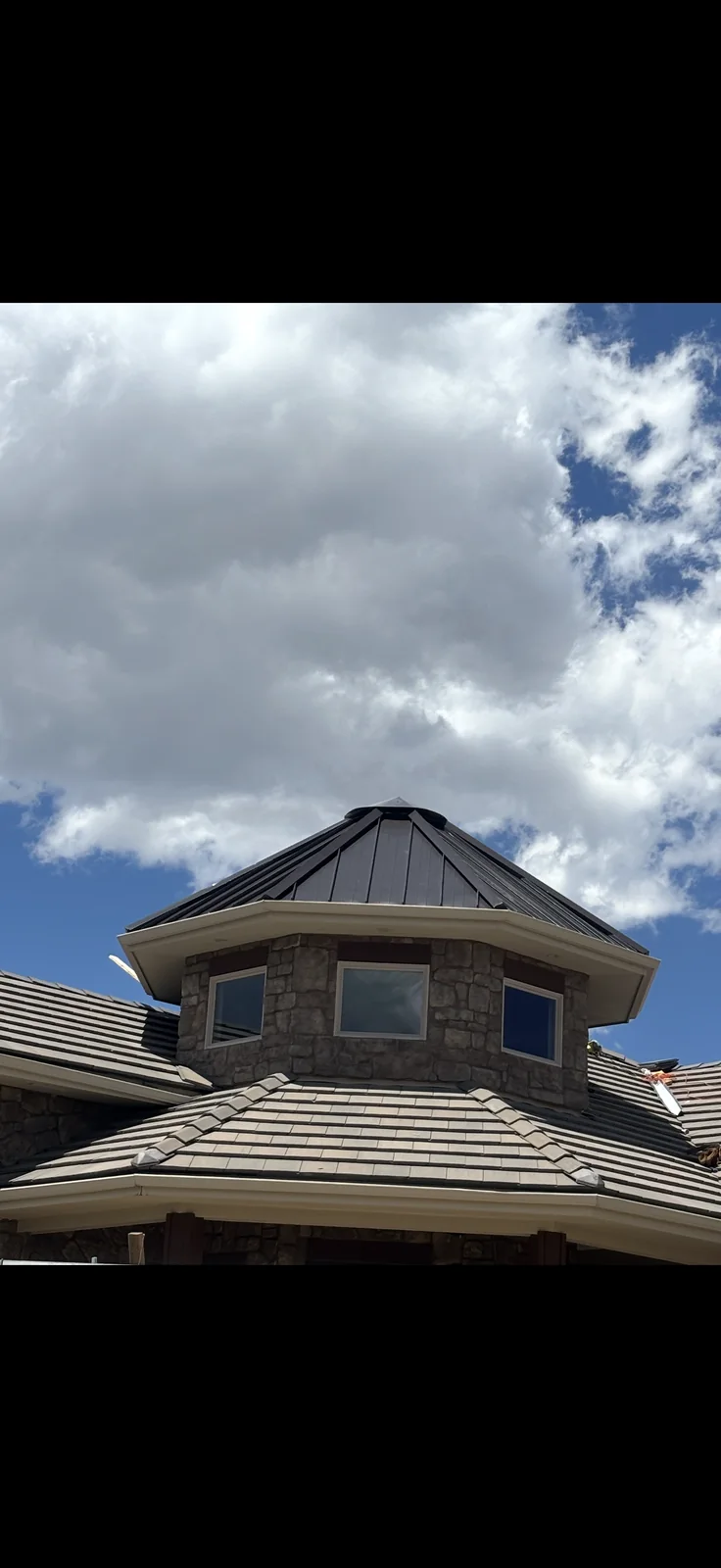 Front view of a dark standing-seam metal turret above a gray modular tile-profile roof